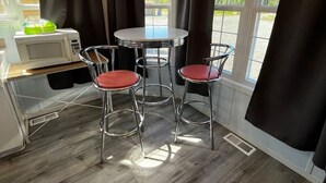 Una cocina compacta con microondas, una mesita y dos taburetes altos.