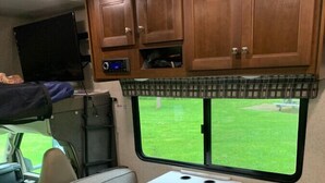 Un intérieur de camping-car compact comprenant un coin cuisine, un espace repas et une fenêtre donnant sur une cour verdoyante.