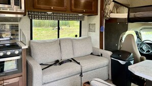Un intérieur de camping-car compact comprenant un coin cuisine, un canapé et une fenêtre donnant sur l’extérieur.