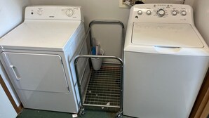 A laundry area with two white washing machines, a metal drying rack, and a trash bin. - RV Site with Full Hookups (Sterling)