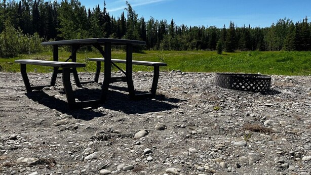A picnic table with benches on a gravel surface, surrounded by a forested area. - RV Site with Full Hookups (Sterling)