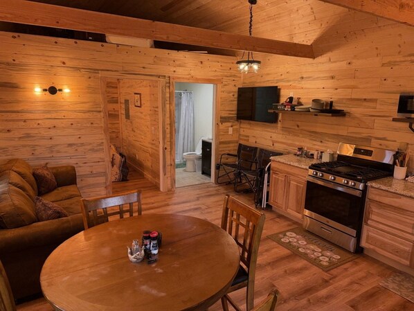 A cozy wooden cabin interior with a dining area, kitchen, and a visible bathroom.