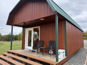 En hyggelig træhytte med veranda, to stole og et bord.