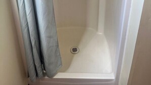 A shower stall with a white door, a visible drain, and a red fire extinguisher mounted on the wall. - RV Site with Full Hookups (Sterling)
