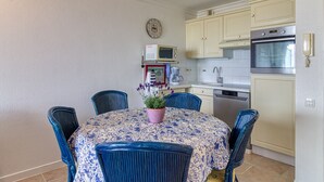 A dining area with a table set for four, surrounded by blue chairs, a potted plant, and a microwave above the table. - Les Goélands - Vue mer à moins d'1 Km de la plage (Bray-Dunes)