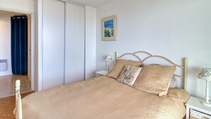 A bedroom with a bed, a nightstand, a lamp, a picture on the wall, and a door leading to another room. - Les Goélands - Vue mer à moins d'1 Km de la plage (Bray-Dunes)