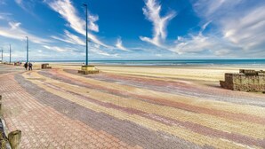 A beach promenade with patterned paving, a clear sky, and a distant view of the sea. - Les Goélands - Vue mer à moins d'1 Km de la plage (Bray-Dunes)