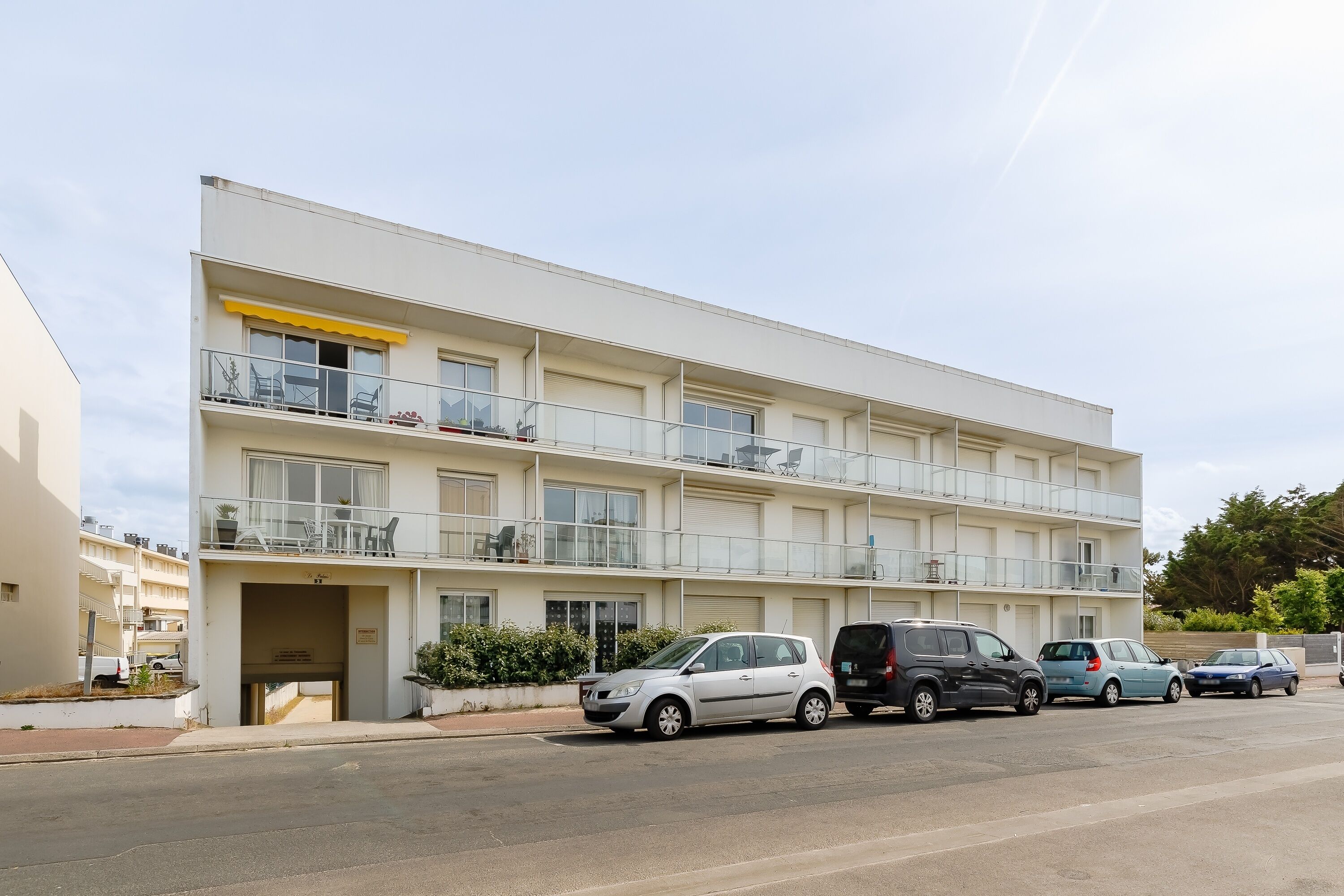 Un immeuble résidentiel à plusieurs étages, doté de balcons et d’un espace de stationnement à l’avant.