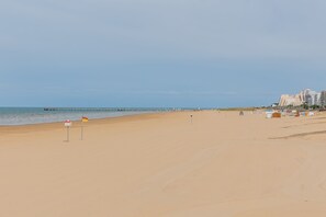 Ein weiter Sandstrand mit blauem Himmel, einigen Flaggen und Gebäuden im Hintergrund.