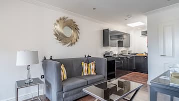 Uma sala de estar moderna com um sofá cinzento, uma mesa de centro de vidro e um espelho decorativo na parede.