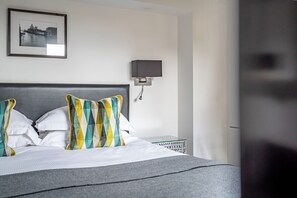 A neatly made bed with white and striped pillows, a grey headboard, and a framed picture of a cityscape on the wall. - Strozzi Palace Luxury Boutique Suites (Cheltenham)