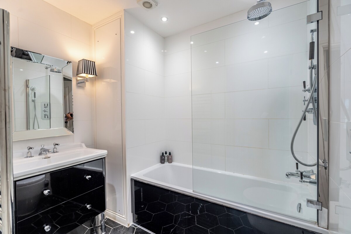 A modern bathroom with a glass-enclosed shower, a white sink with a black marble countertop, and a black vanity with drawers.