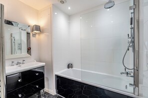 A modern bathroom with a glass-enclosed shower, a white sink with a black marble countertop, and a black vanity with drawers. - Strozzi Palace Luxury Boutique Suites (Cheltenham)