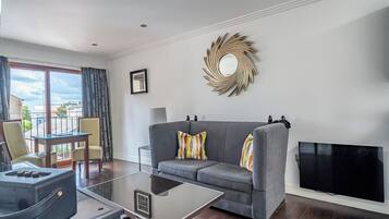Una sala de estar moderna con un sofá gris, una mesa de centro de vidrio, un televisor de pantalla plana y un espejo decorativo en la pared.