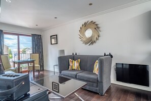 Ein modernes Wohnzimmer mit einem grauen Sofa, einem Glastisch, einem Flachbildfernseher und einem dekorativen Spiegel an der Wand.