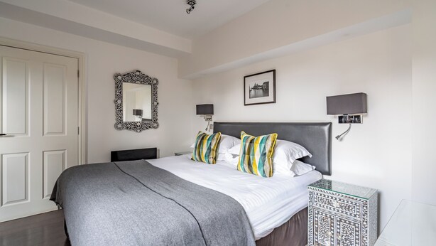 Een keurig opgemaakt slaapkamer met een groot bed, een nachtkastje, een spiegel en een wandlamp.