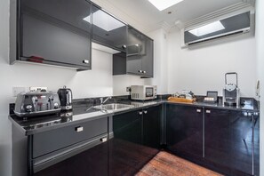 A modern kitchen with dark cabinetry, a stainless steel sink, a microwave, a toaster, and a coffee machine. - Strozzi Palace Luxury Boutique Suites (Cheltenham)