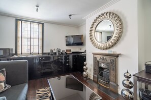 Una sala de estar moderna con chimenea, un espejo grande y una zona de cocina con armarios negros y un televisor de pantalla plana.