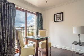 Une pièce comprenant une table à manger avec un plateau en verre, deux chaises, une petite table d’appoint avec une lampe et un tableau encadré accroché au mur.