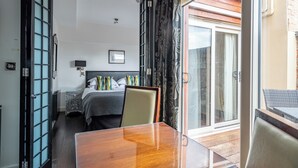 Een hotelkamer met een houten tafel, een bed met een grijs hoofdeinde, een nachtkastje en een uitzicht op buiten door een glazen deur.