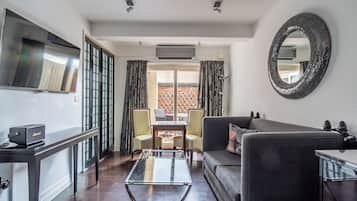 Una sala moderna con una mesa de centro de vidrio, un sofá negro, un televisor montado en la pared y un comedor con mesa y sillas.