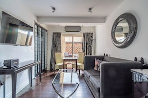 Una sala moderna con una mesa de centro de vidrio, un sofá negro, un televisor montado en la pared y un comedor con mesa y sillas.