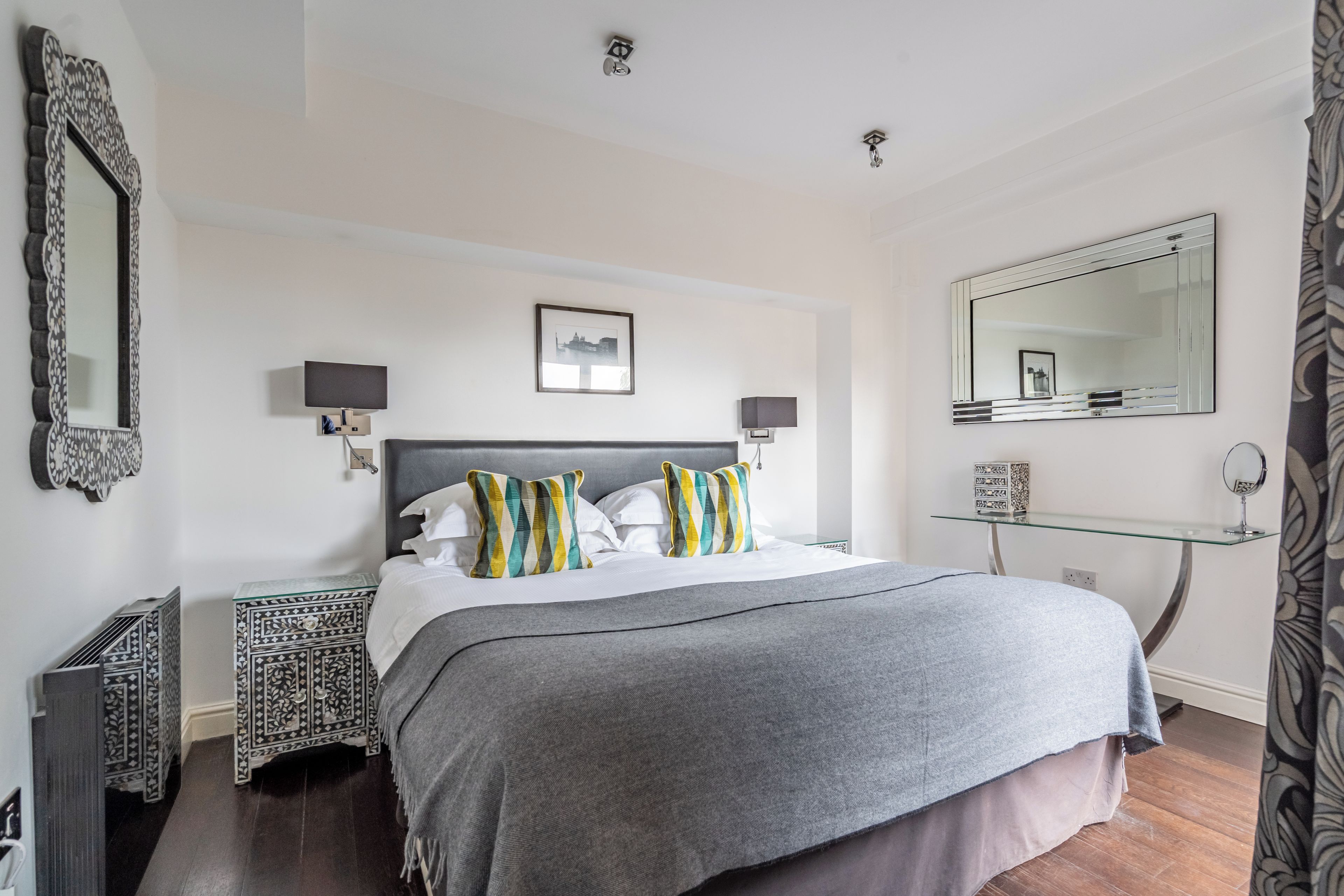 A neatly arranged bedroom with a large bed, two bedside tables, a glass shelf, and a mirror.