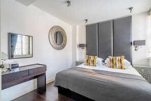 Ein modernes Schlafzimmer mit einem großen Bett, einem Nachttisch, einem Spiegel und einem an der Wand befestigten Fernseher.