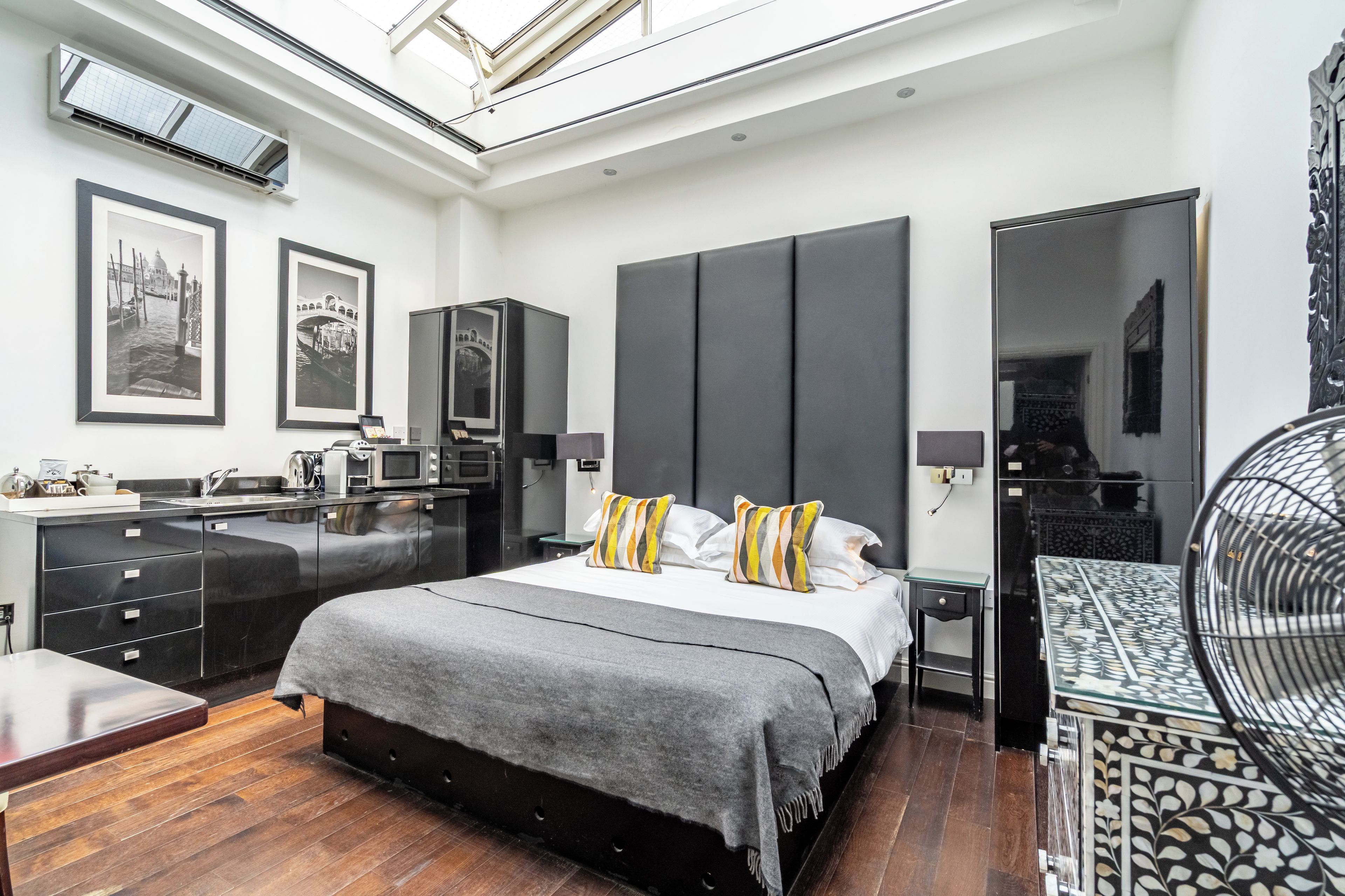 A modern bedroom with a large bed, a built-in wardrobe, a desk, and a dining table.