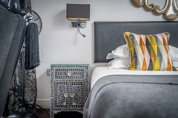 A neatly made bed with a striped pillow, a wall-mounted fan, and a patterned nightstand. - Strozzi Palace Luxury Boutique Suites (Cheltenham)