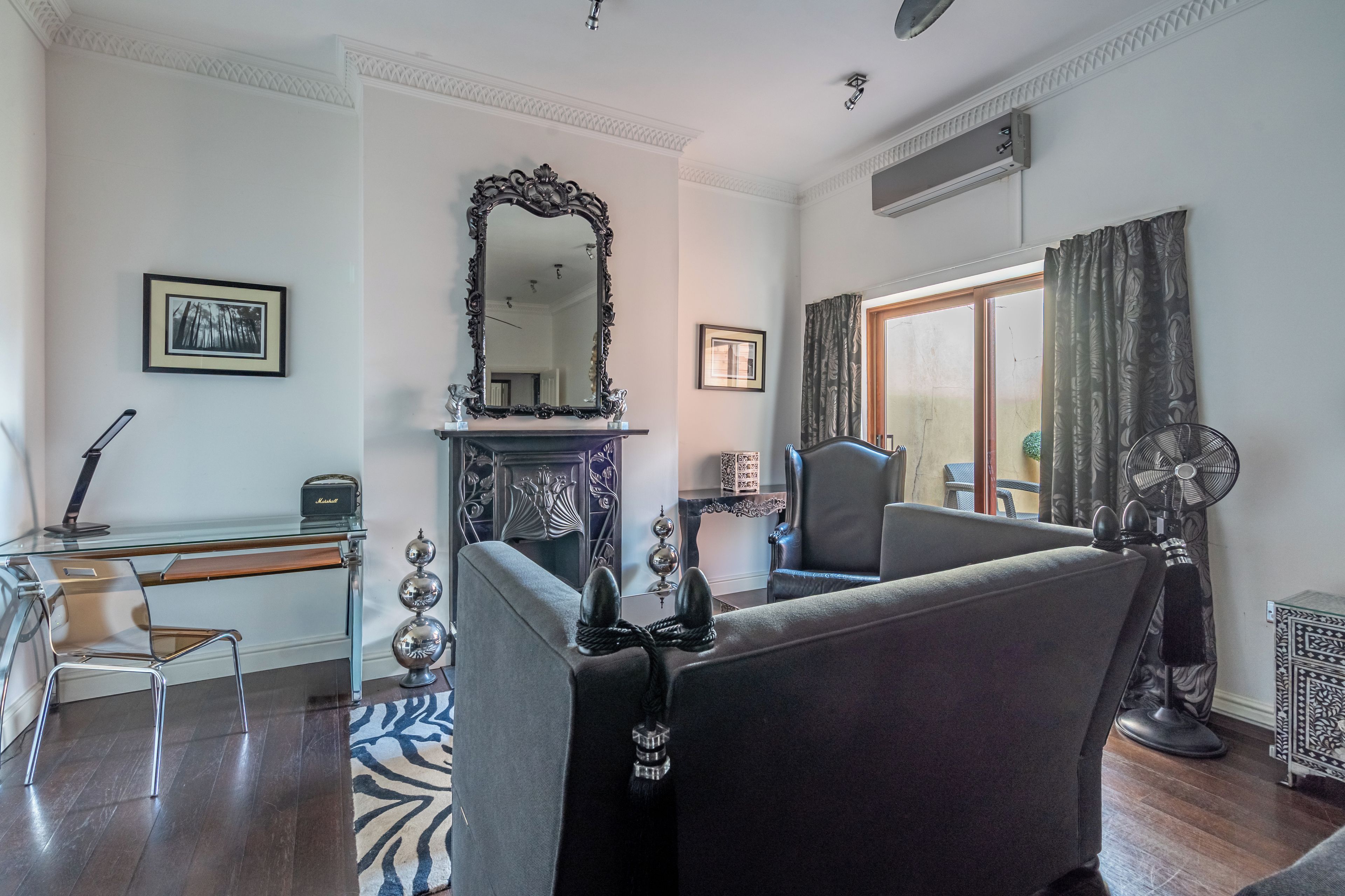 A room with a fireplace, a large mirror, a sofa, a chair, a desk, and a fan.