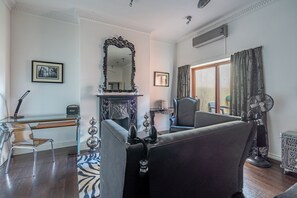 A room with a fireplace, a large mirror, a sofa, a chair, a desk, and a fan. - Strozzi Palace Luxury Boutique Suites (Cheltenham)