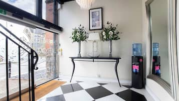 A hotel lobby with a checkered floor, a console table with two vases, a water dispenser, and a chandelier.