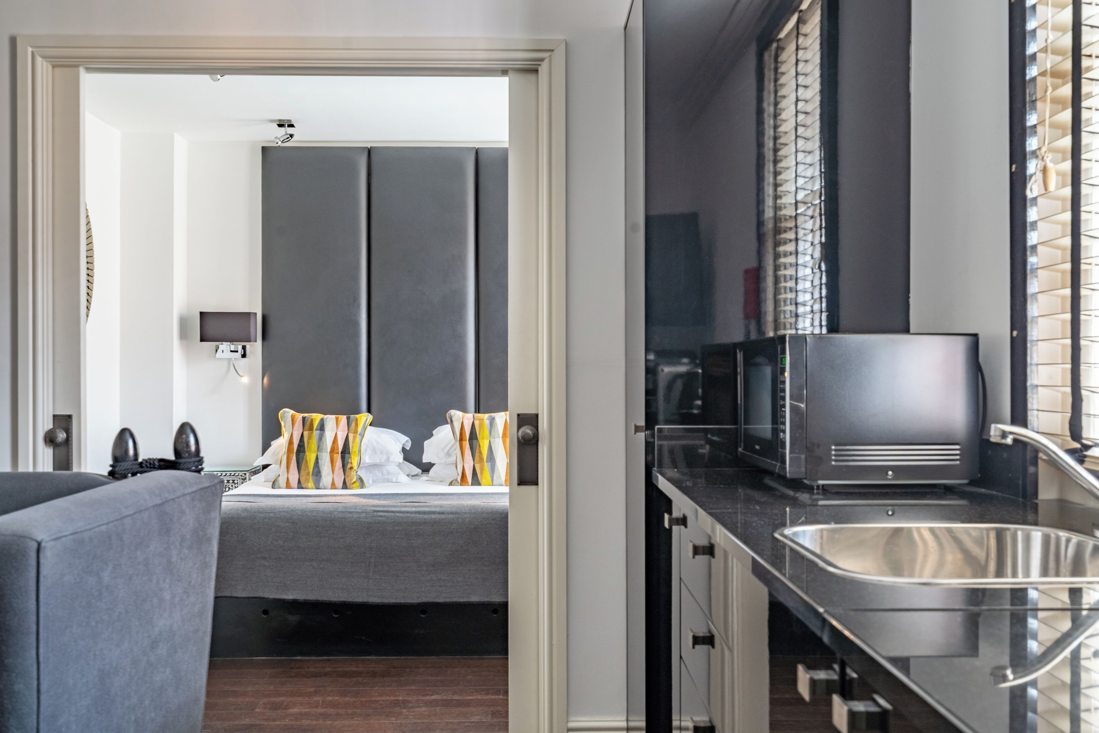 Una habitación de hotel moderna con una cama, un sofá, una kitchenette con microondas y un lavabo.