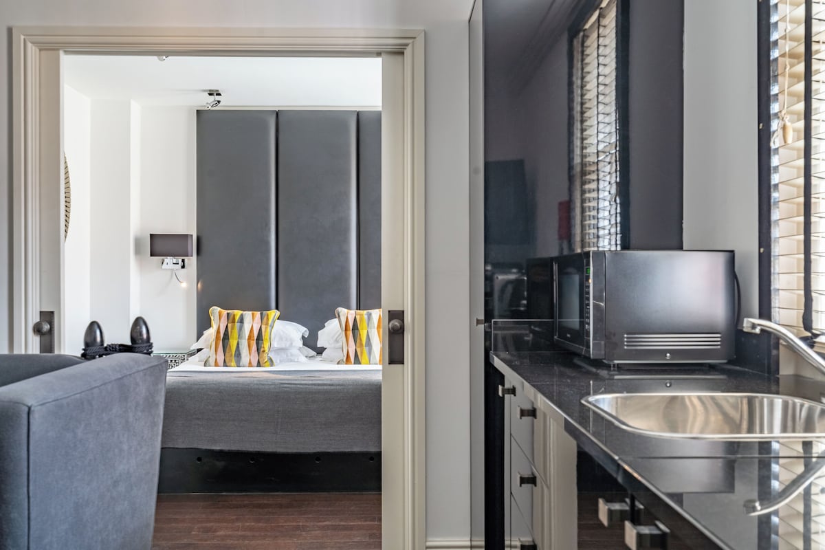 Una habitación de hotel moderna con una cama, un sofá, una kitchenette con microondas y un lavabo.