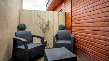 An outdoor seating area with two wicker chairs and a small table, surrounded by wooden walls and a concrete fence.