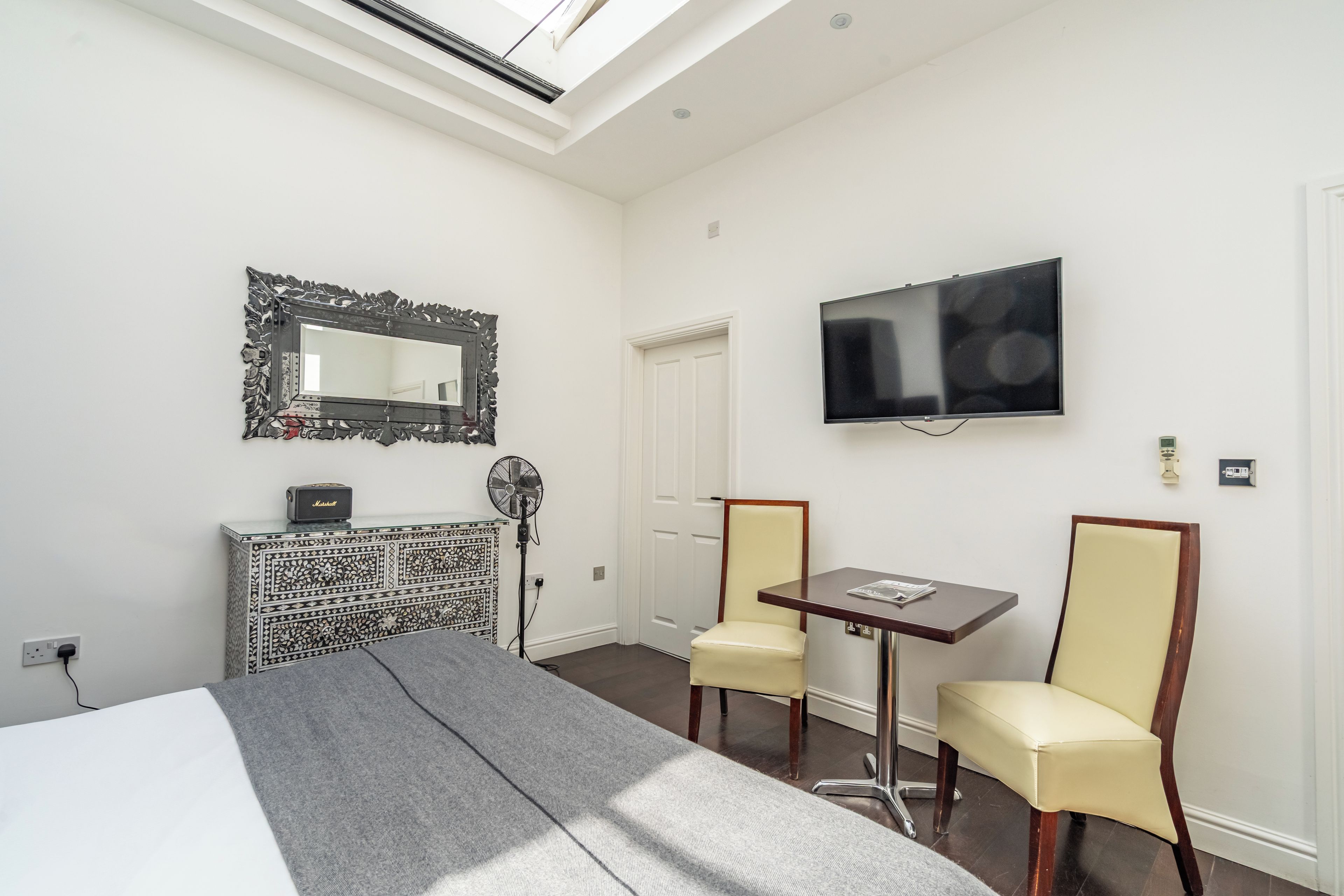 A hotel room with a bed, a desk, two chairs, a TV, a mirror, and a patterned cabinet.