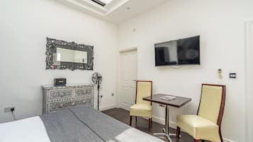 A hotel room with a bed, a desk, two chairs, a TV, a mirror, and a patterned cabinet.