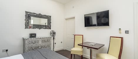 Quarto de hotel com cama, escrivaninha, duas cadeiras, televisão, espelho e armário com padrão.