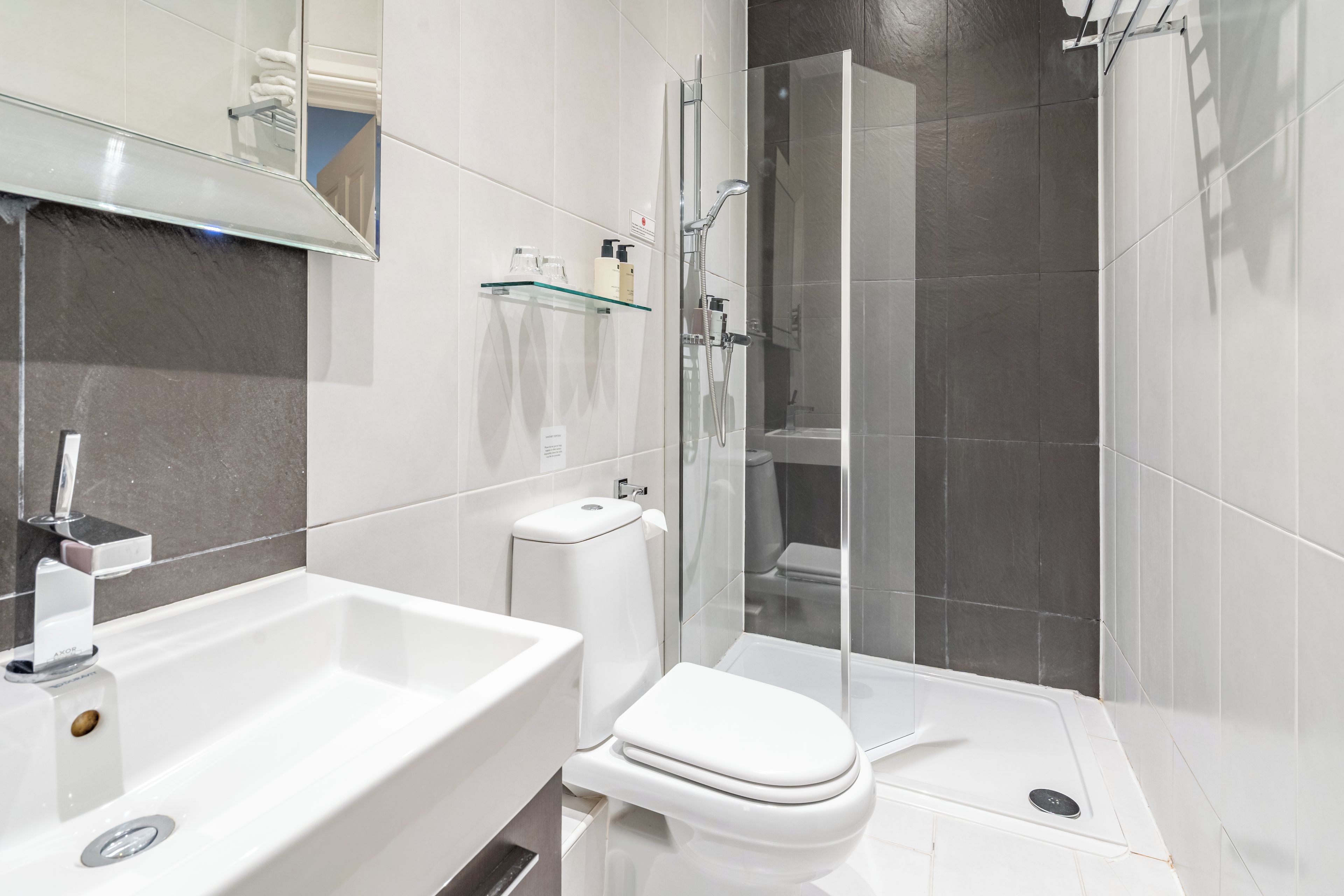Un baño moderno con cabina de ducha de vidrio, un lavamanos blanco y un inodoro.