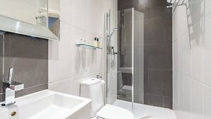 Een moderne badkamer met een douchecabine van glas, een witte wastafel en een toilet.