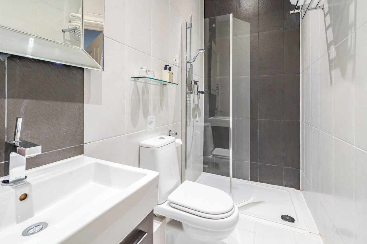 Un baño moderno con cabina de ducha de vidrio, un lavamanos blanco y un inodoro.