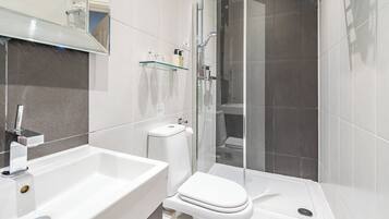Un baño moderno con cabina de ducha de vidrio, un lavamanos blanco y un inodoro.