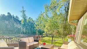 A deck with wicker furniture and a colorful rug, overlooking a grassy area and trees.