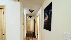 A hallway with wooden flooring, white walls, and a black framed picture on the right.