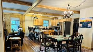 A cozy, well-lit kitchen with wooden cabinets, a dining area with a table set for four, and a chandelier above.