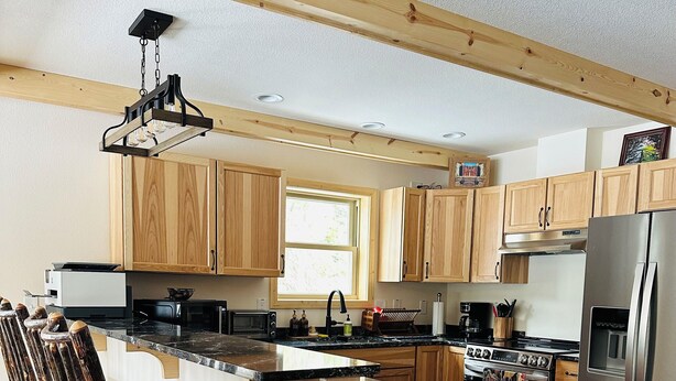 A modern kitchen with wooden cabinets, a stainless steel refrigerator, a built-in oven, and a bar stool area.