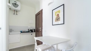 A small kitchenette with a white table and bench, a framed picture of Florence, and a door. - Pinzochere 16 - Studio Apartment, Sleeps 2 (Firenze)
