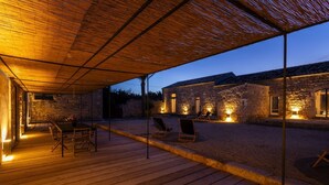A wooden deck with outdoor seating and a stone building in the background. - Casa Sisti - Villa with heated pool (Rosolini)