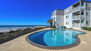 Una piscina con vista al océano, un edificio con balcones y un entorno frente a la playa.